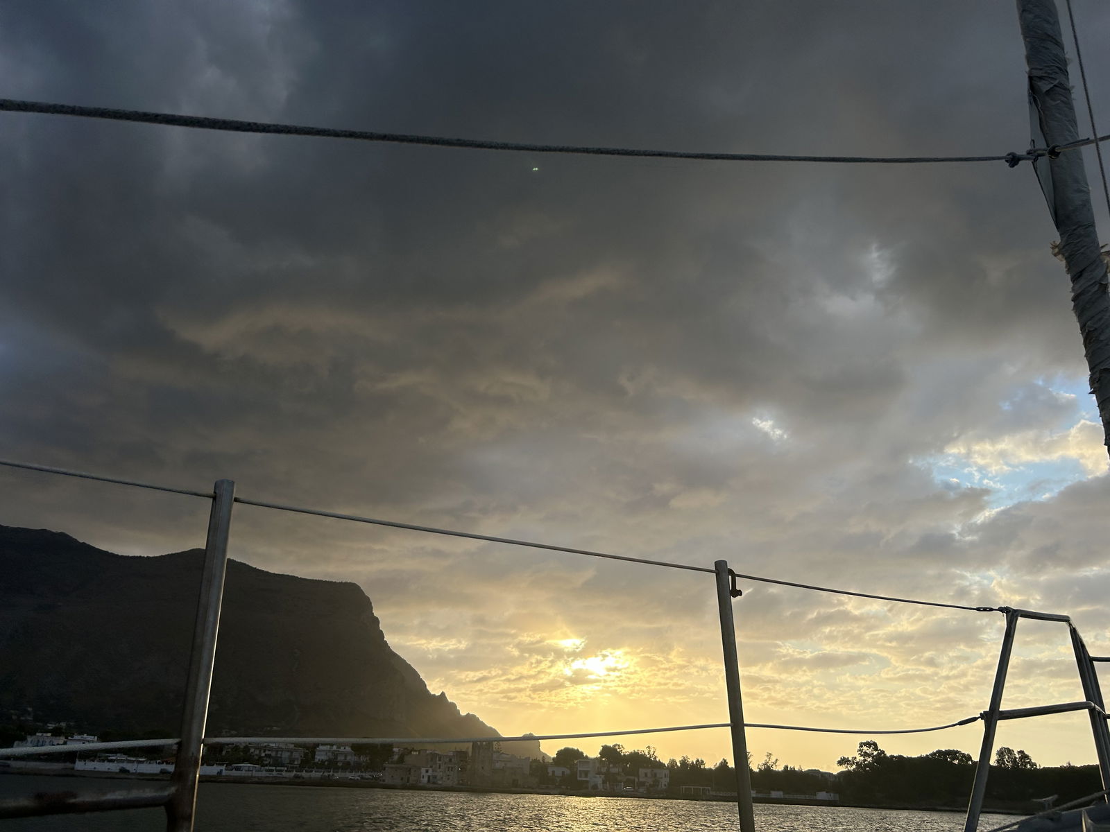 Západ slunce s dramatickými mraky nad mořem, pohled přes loď.